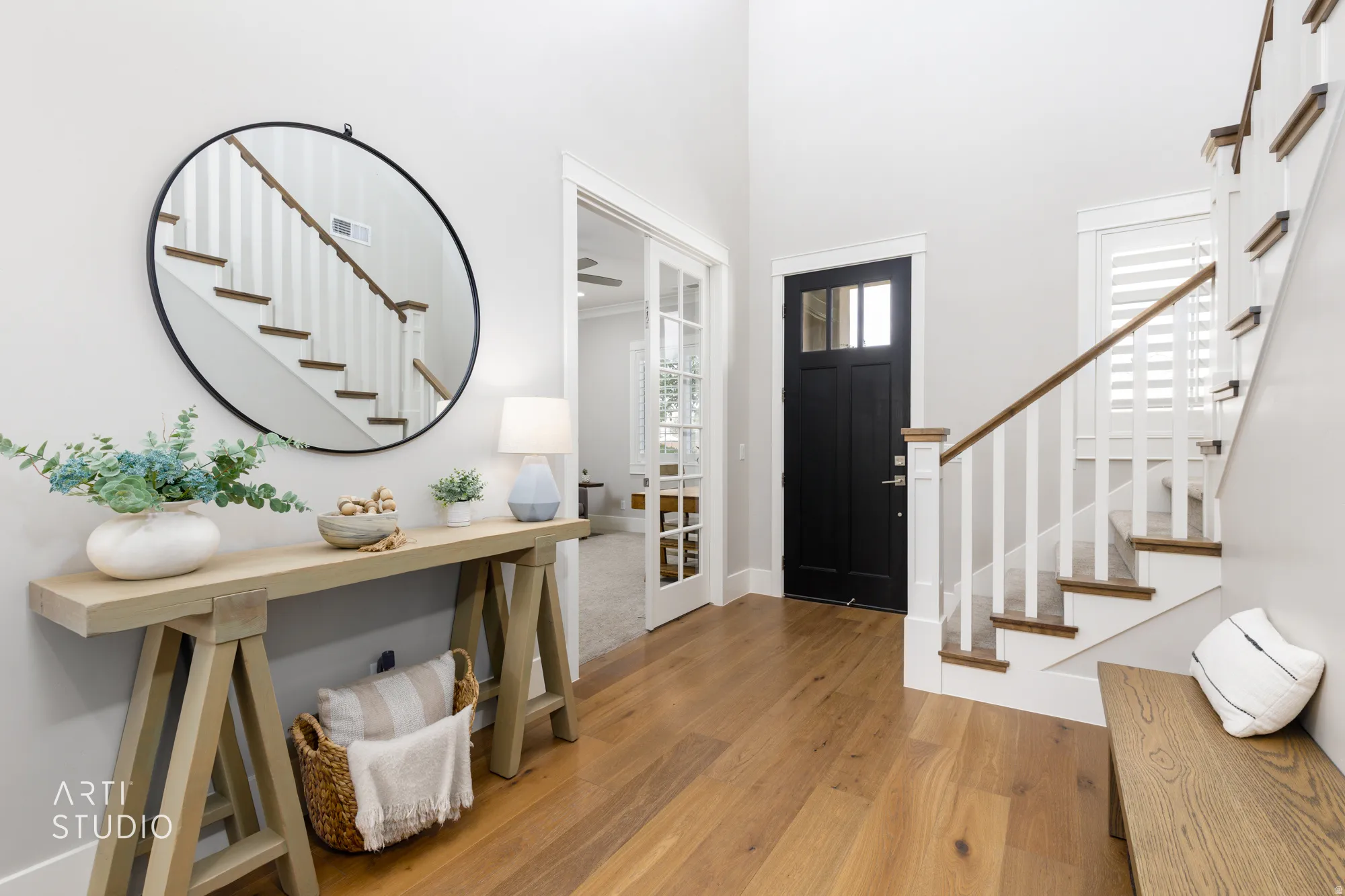 Bright entryway featuring wood-finish flooring, a dark-paneled front door with clear glass inserts, and a staircase with white risers and wood treads