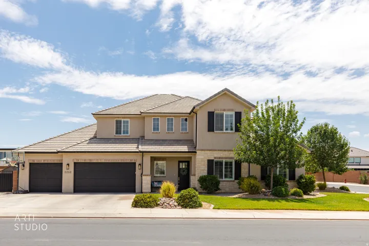 Two-story stucco and stone-clad residence featuring a tiled roof and integrated three-car garage