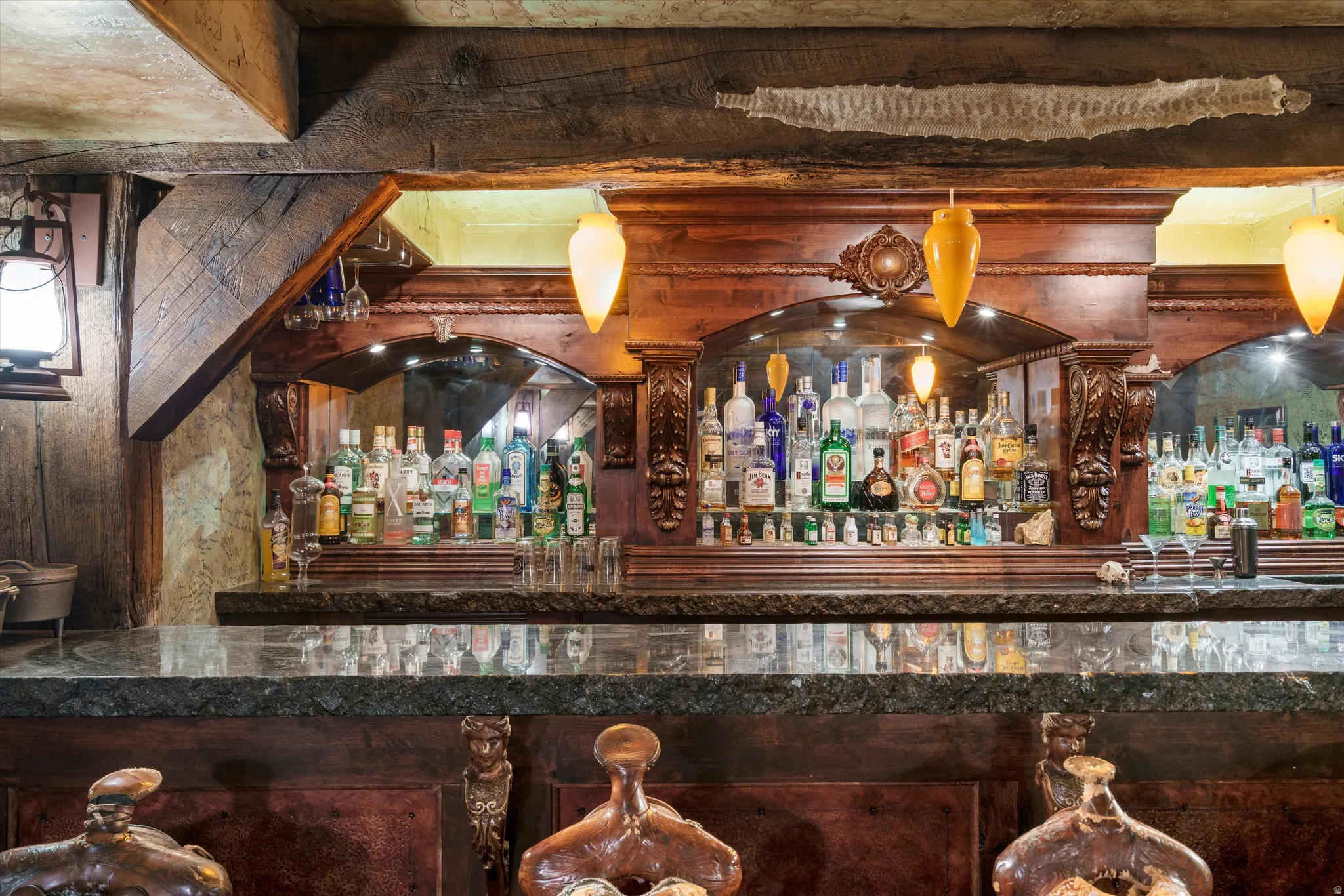 Custom built-in bar featuring a granite countertop, carved wood detailing, arch-top mirrored backsplashes, and integrated pendant lighting