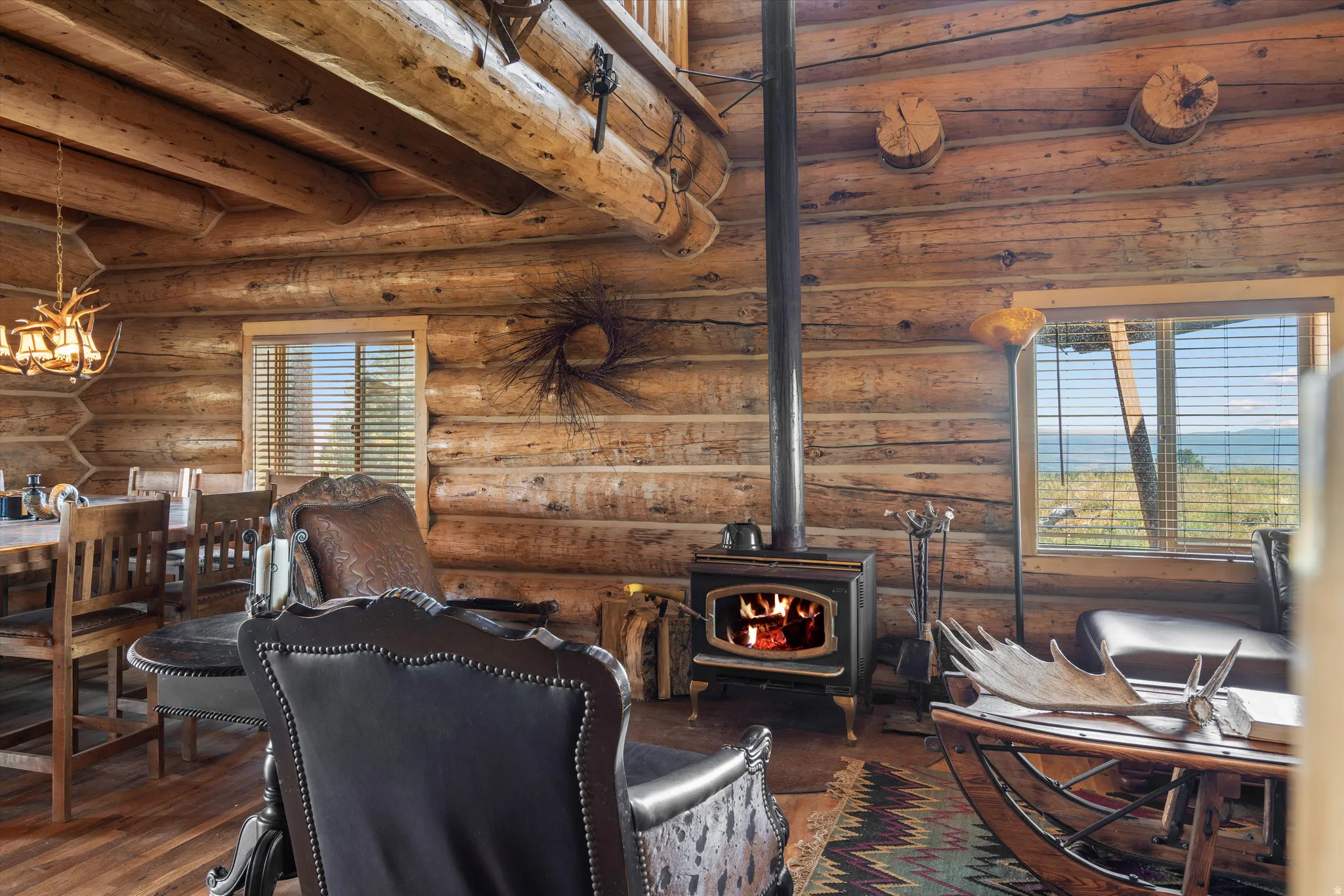 Expansive wood-paneled interior featuring a prominent wood-burning stove, exposed log beam ceiling, and durable wood-finish flooring