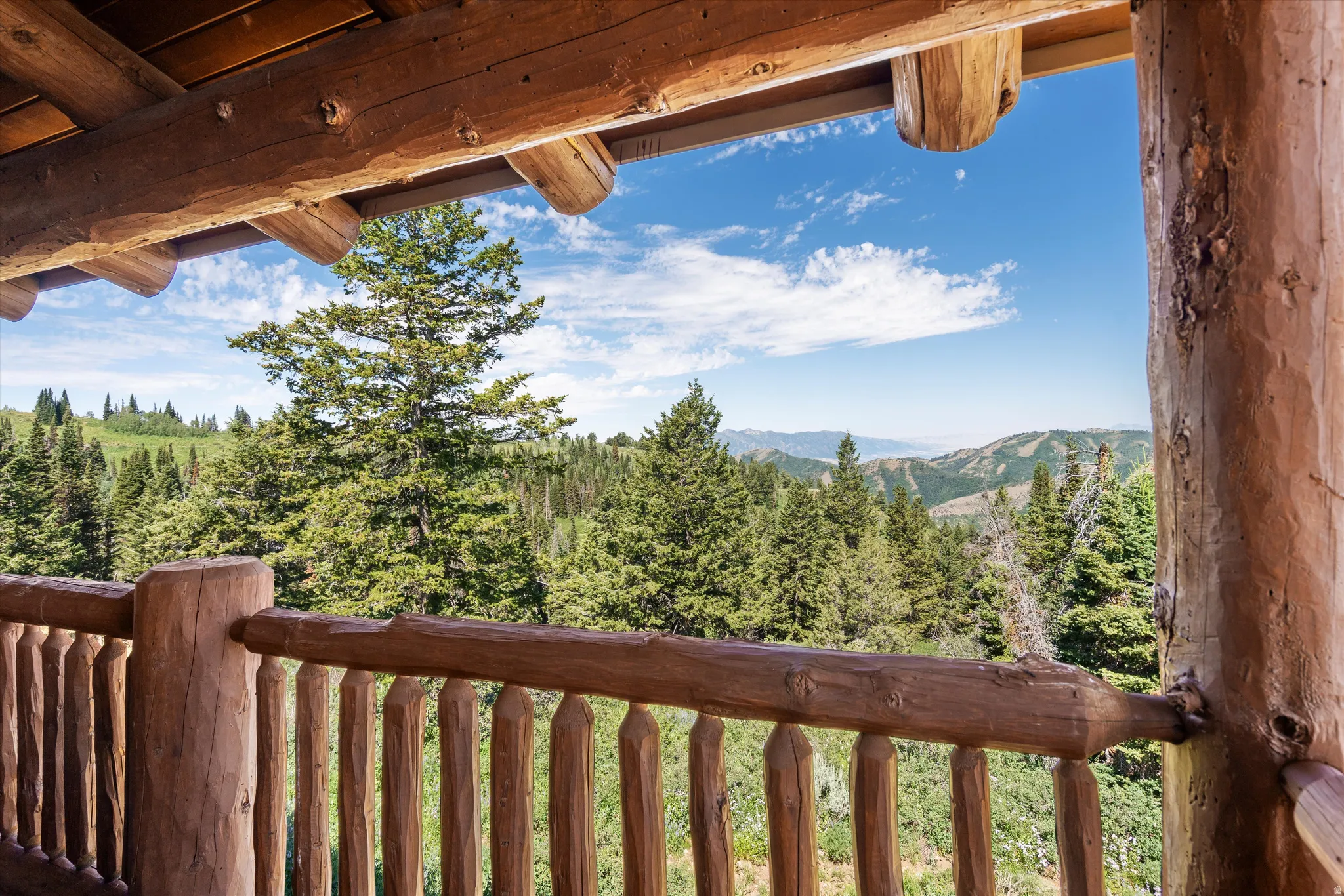 Balcony with log railing and support beams featuring expansive mountain and tree-filled scenery