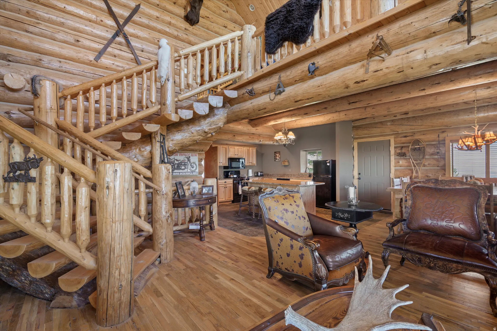 Open-concept log home featuring a grand log spiral staircase, exposed log beam ceilings, wood-finish flooring, and a kitchen with wood cabinetry
