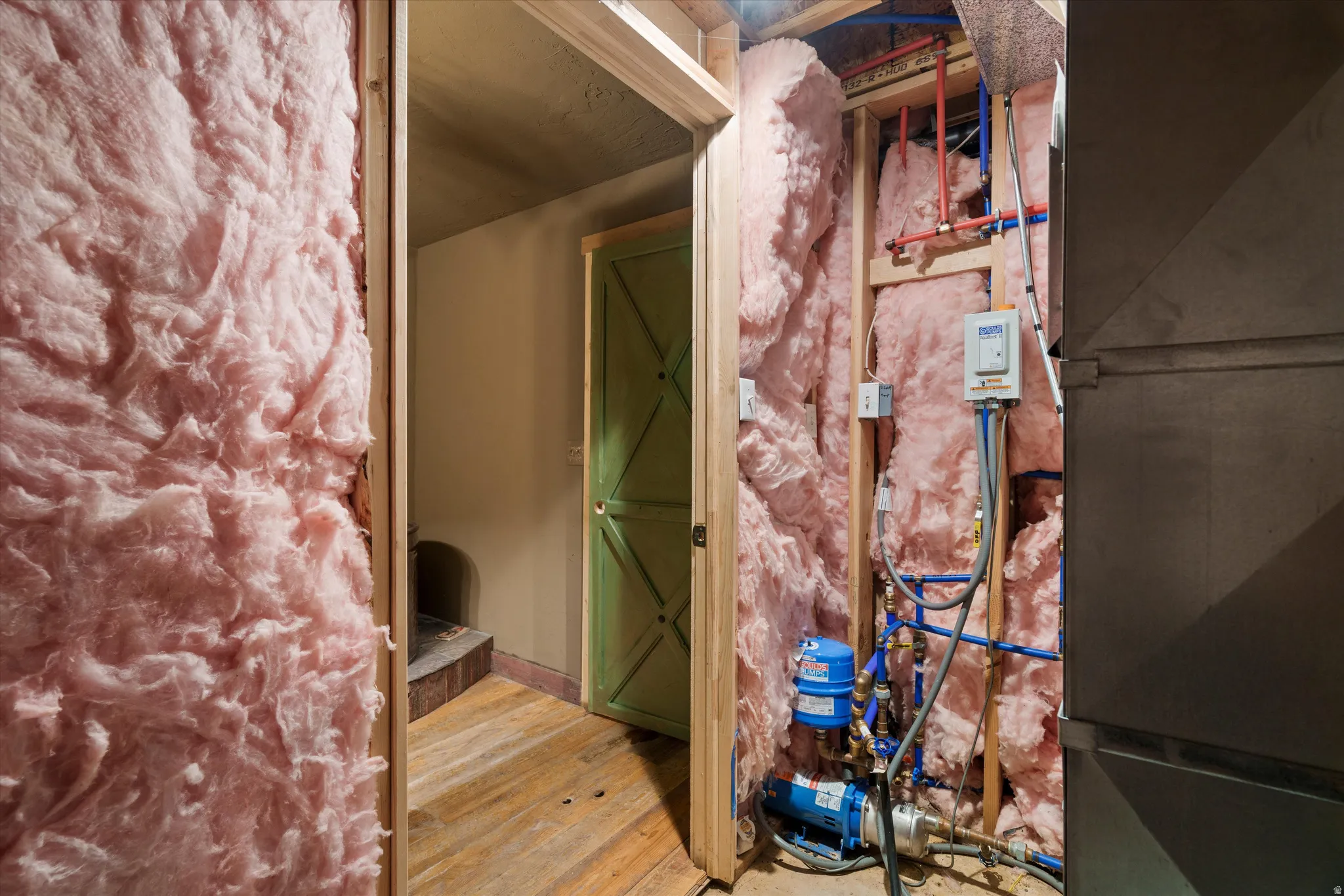 Exposed insulation and framing revealing internal mechanical systems including plumbing and electrical components