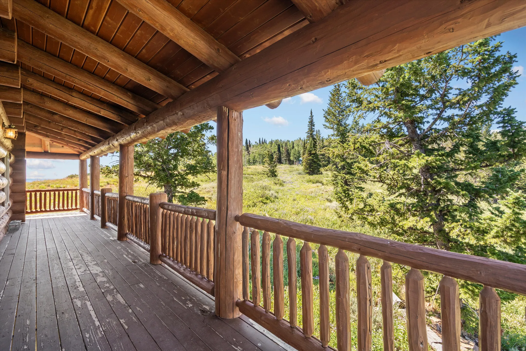 Expansive covered porch featuring a natural wood ceiling, wood-finish flooring, log beam supports, and a log railing system
