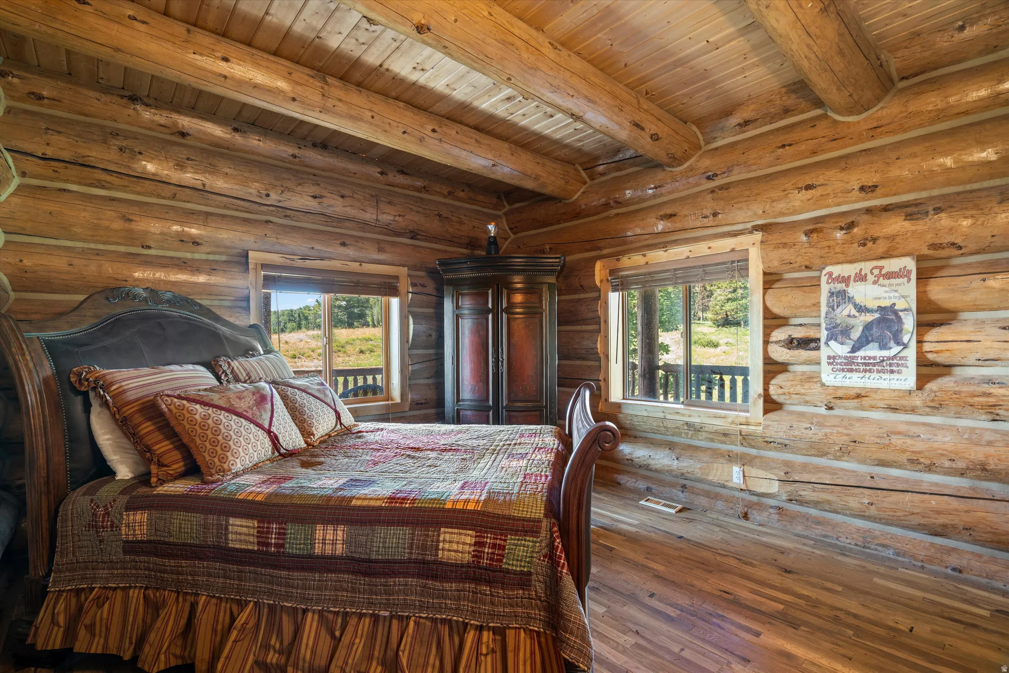 Log cabin interior featuring exposed log walls and ceiling beams, wood-finish flooring, and two windows with natural wood trim