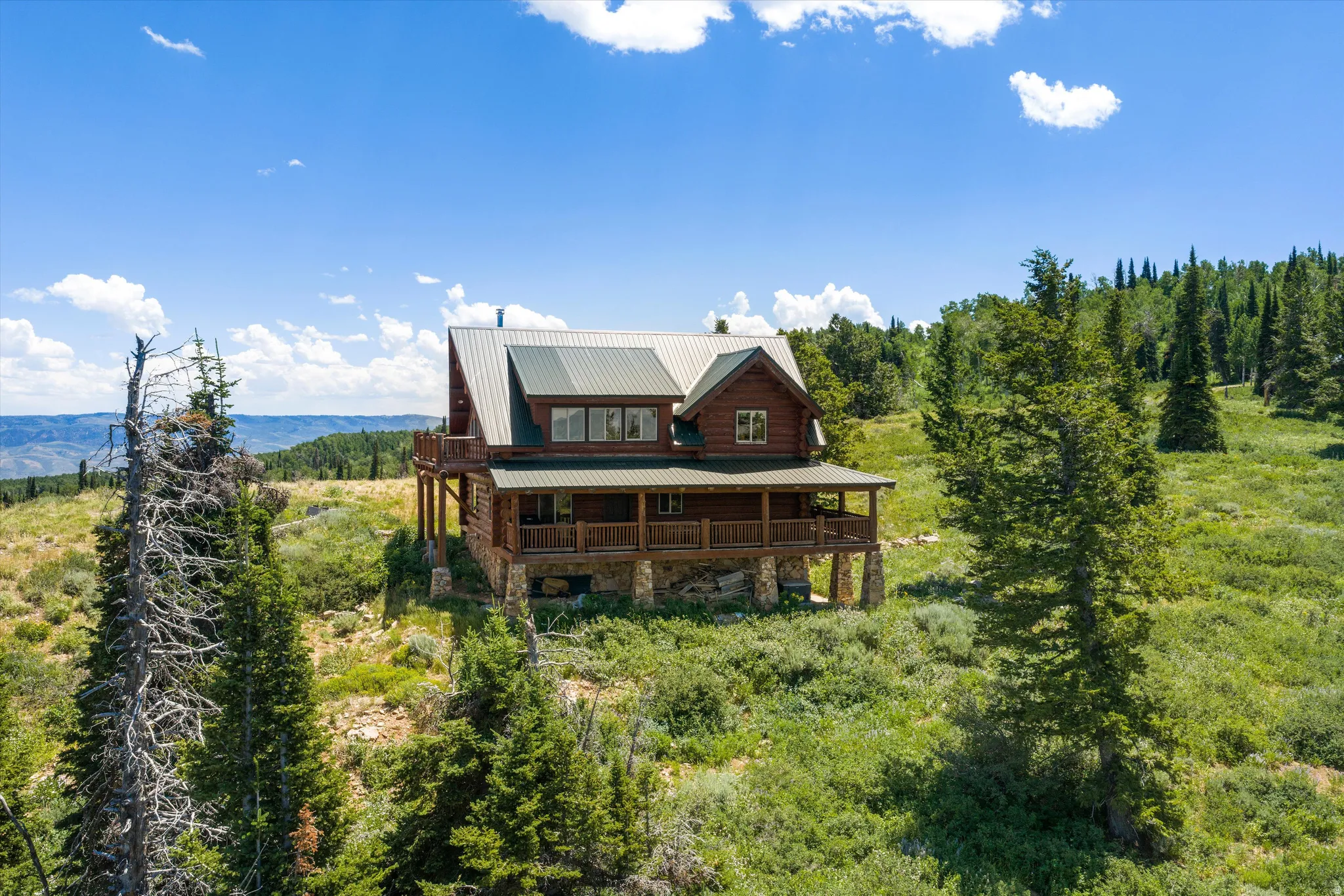 Log cabin residence featuring a metal roof, stone foundation, multi-level decking, and a balcony