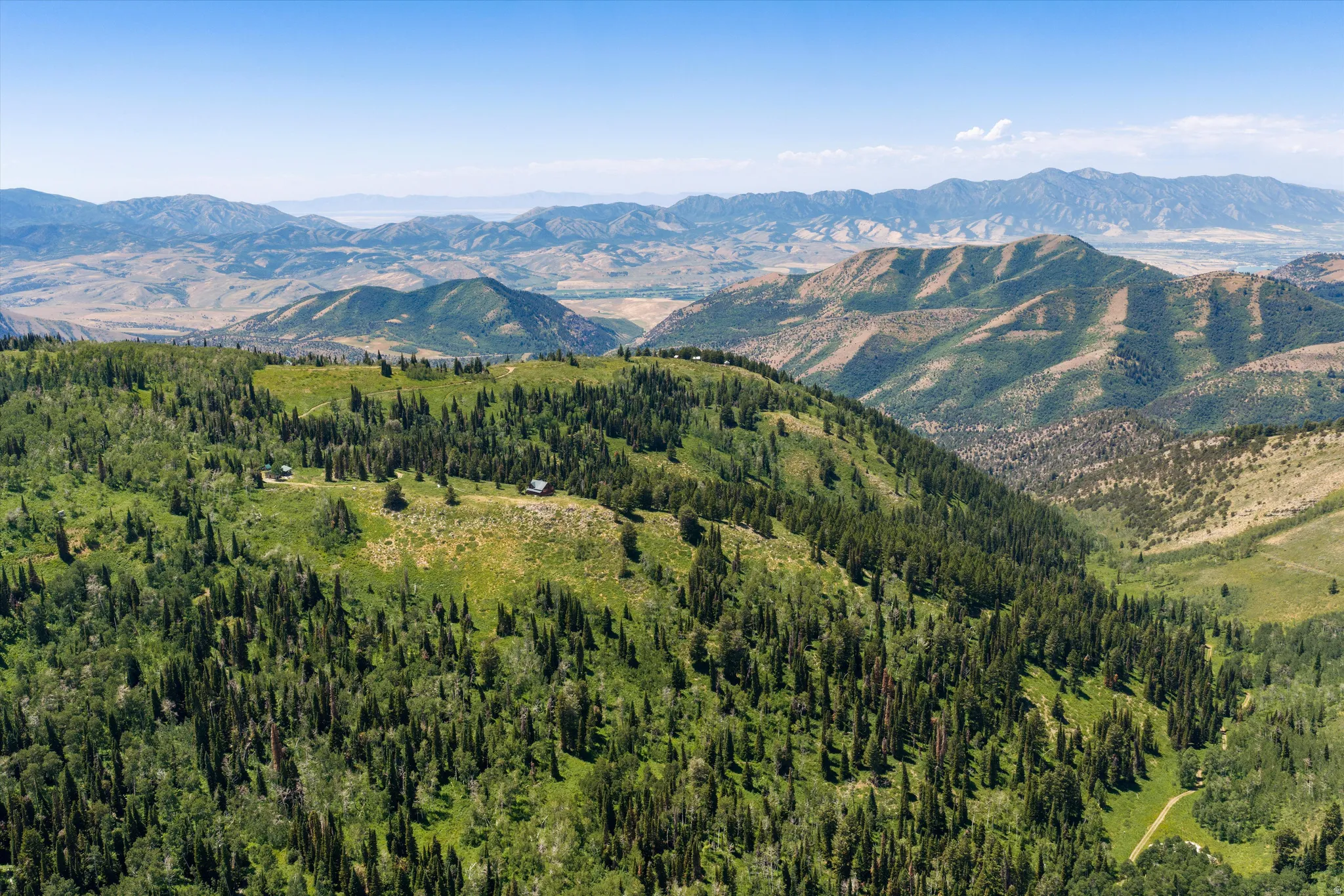 Expansive mountain landscape featuring varied terrain, dense evergreen forests, and distant mountain ranges