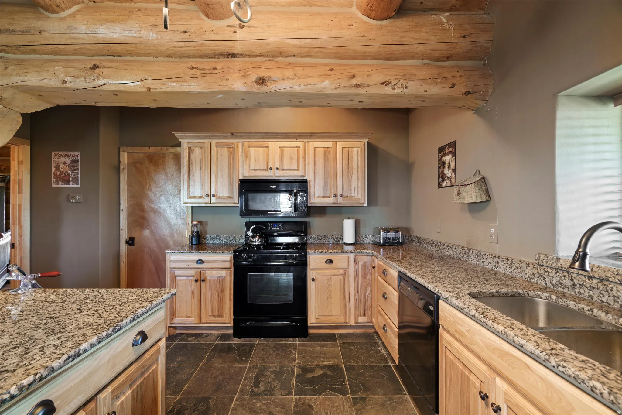 Kitchen featuring visible log beams, slate-tile flooring, light wood cabinetry, and granite countertops
