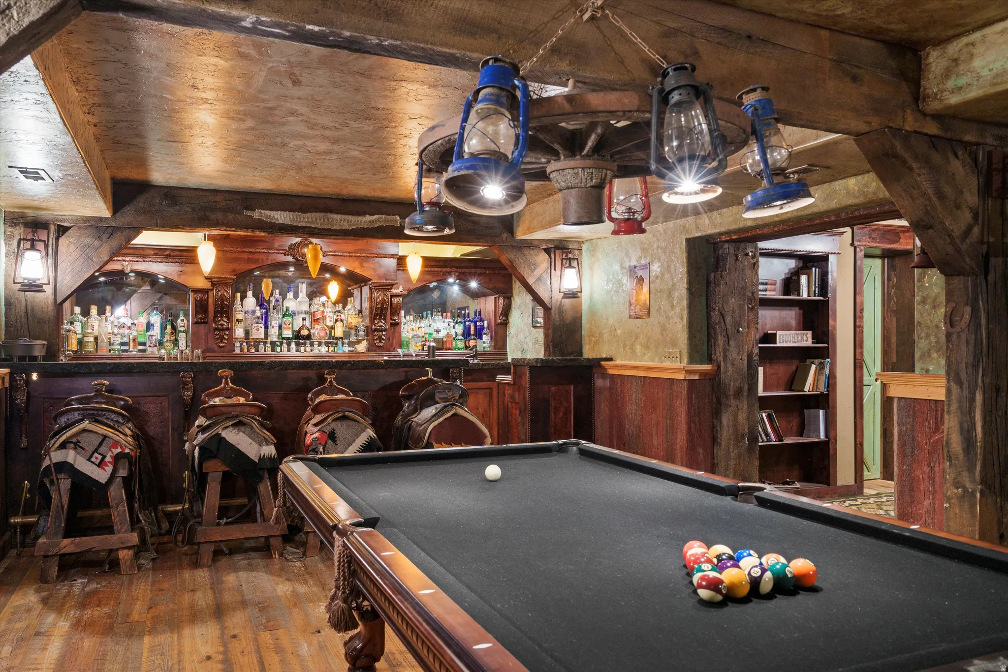 Recreation space featuring a billiards table with dark felt, a fully equipped bar with wood paneling and integrated shelving, textured walls, and wood-finish flooring