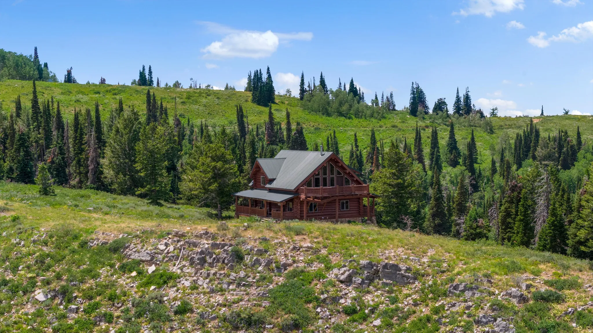 Rustic log cabin exterior with a multi-level design, featuring a covered porch and an upper-level balcony