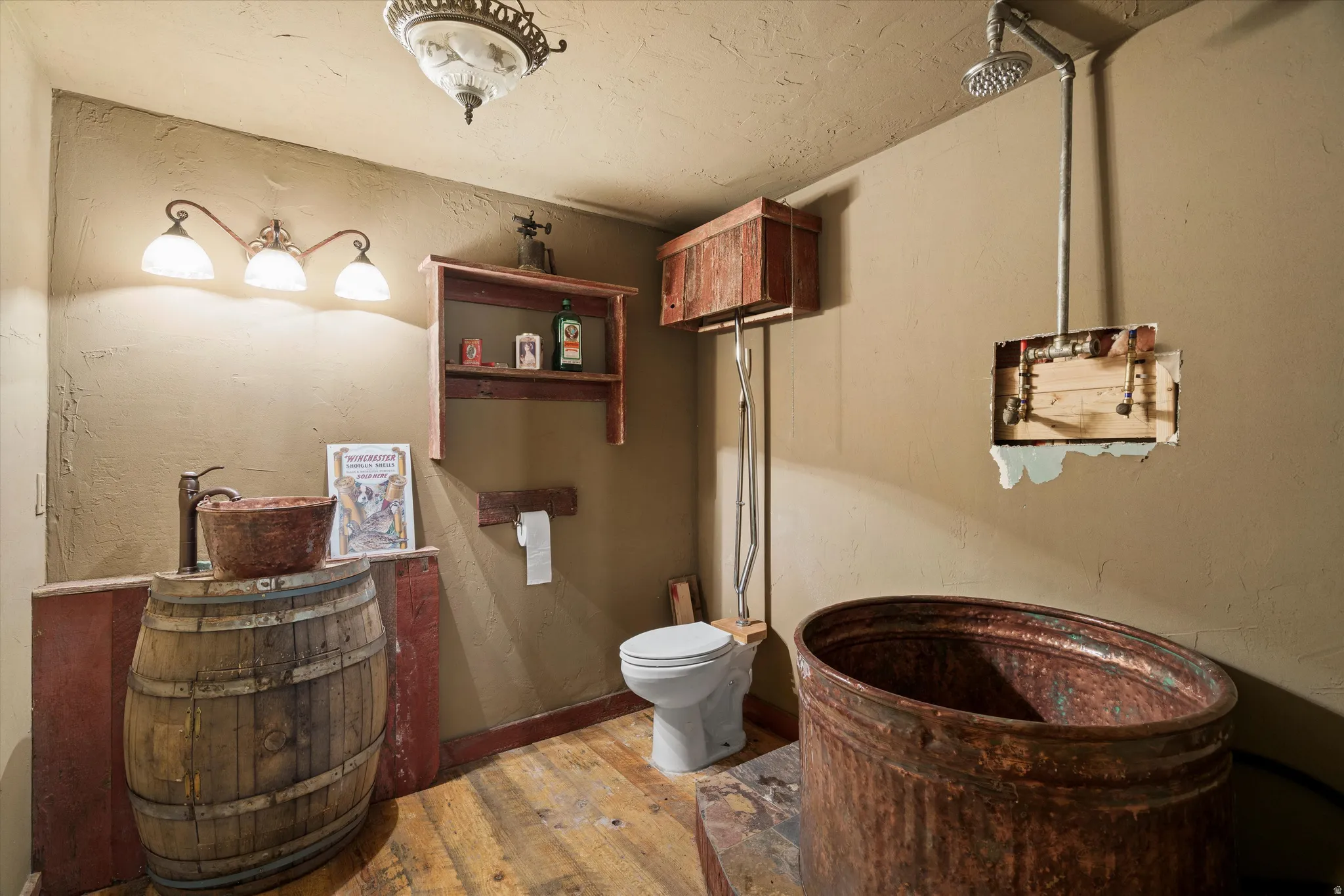 Bathroom featuring a barrel vanity with a basin sink, rustic wood-finish flooring, a wall-mounted toilet, an exposed pipe shower fixture, and a copper soaking tub