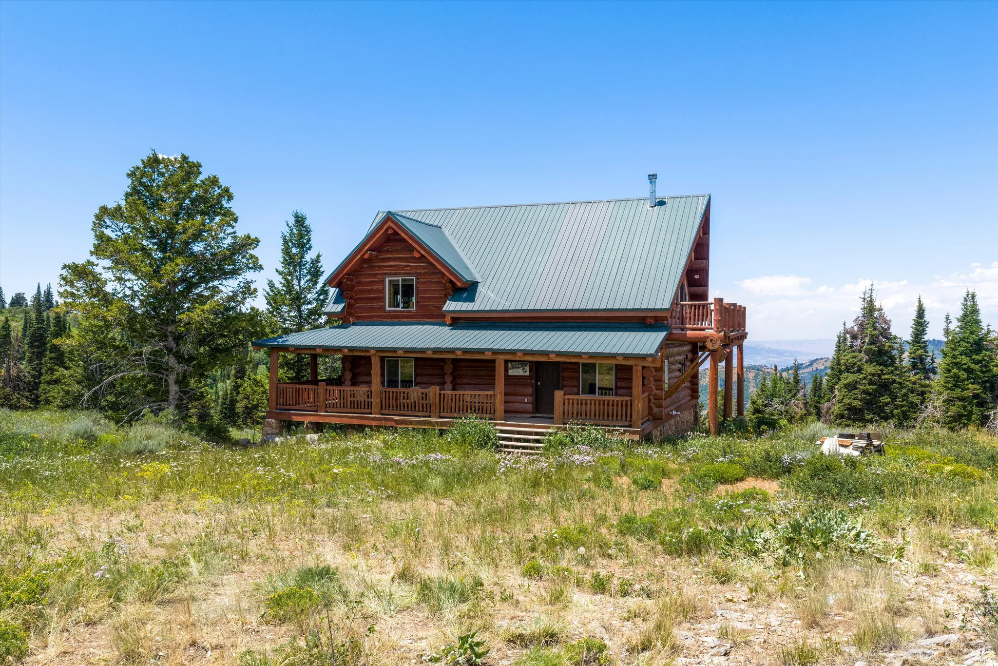 Log cabin exterior featuring a steep-pitched metal roof, full-width covered porch, and an upper-level balcony