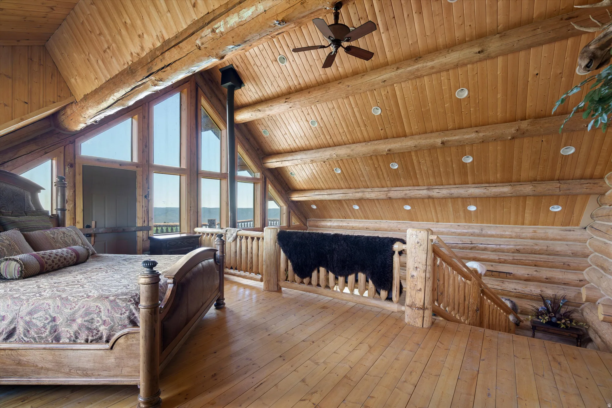 Loft area featuring exposed log beams, wood-plank flooring, and a vaulted wood-paneled ceiling with recessed lighting and a ceiling fan