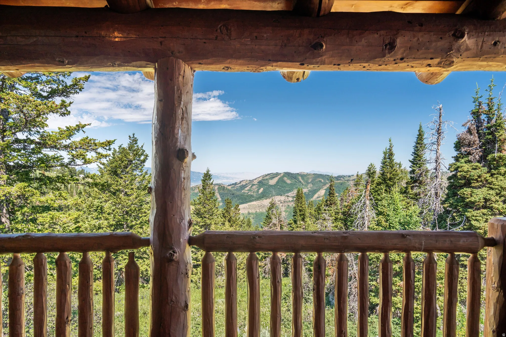 Balcony with natural log construction, log railings, and a mountain landscape featuring abundant evergreen trees