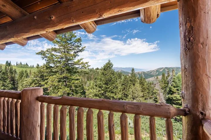 Balcony with log railing and support beams featuring expansive mountain and tree-filled scenery
