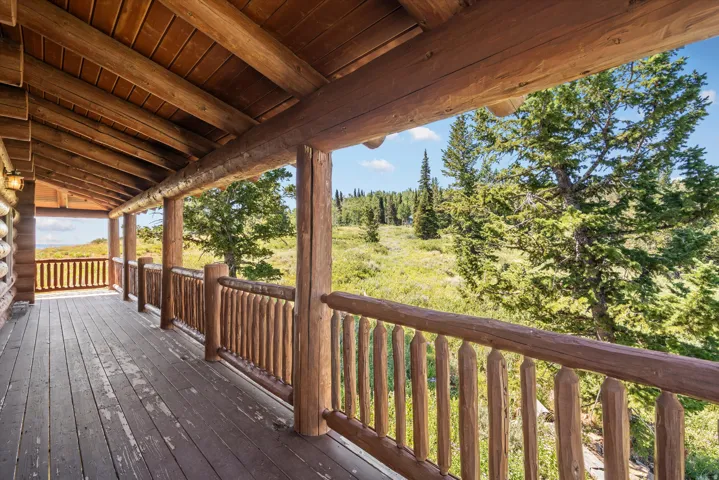 Expansive covered porch featuring a natural wood ceiling, wood-finish flooring, log beam supports, and a log railing system
