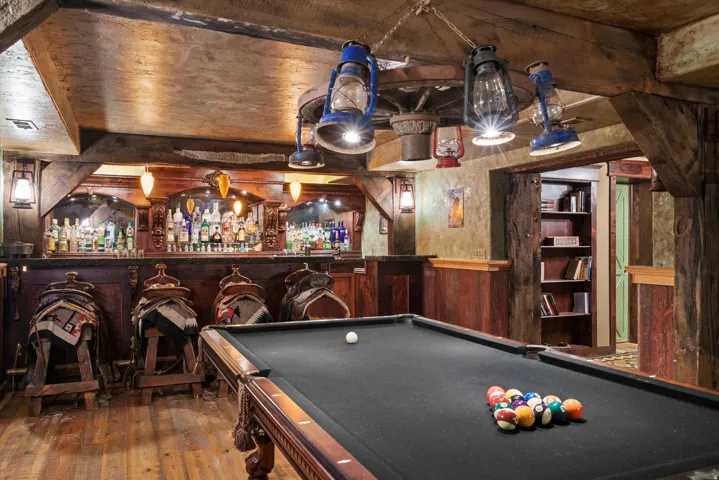 Recreation space featuring a billiards table with dark felt, a fully equipped bar with wood paneling and integrated shelving, textured walls, and wood-finish flooring
