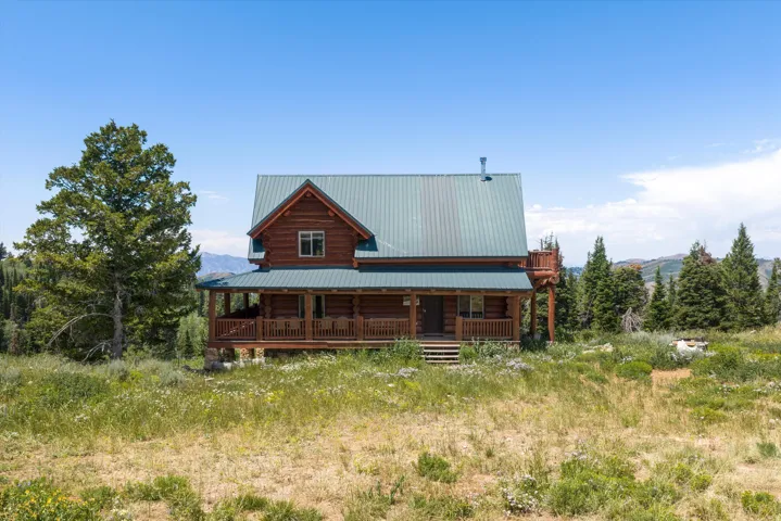 Log cabin exterior featuring a covered porch, metal roof, and upper-level deck