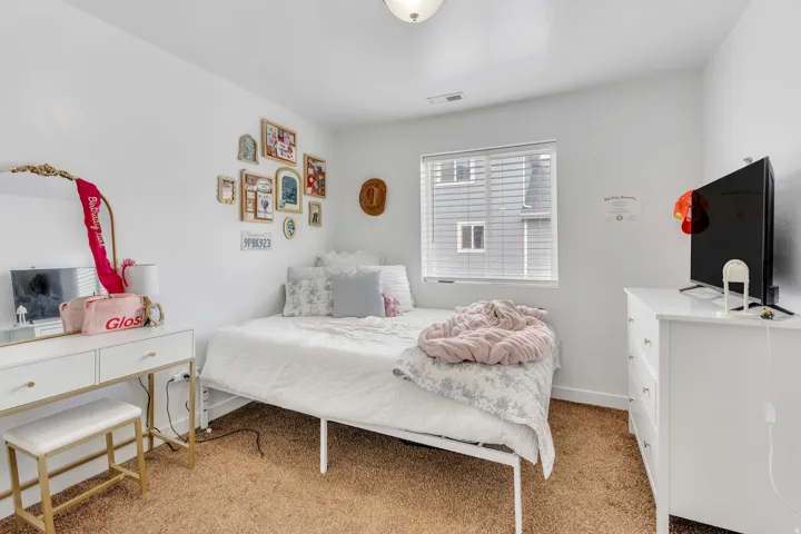 Carpeted bedroom featuring a window with horizontal blinds, white walls, and a ceiling light fixture
