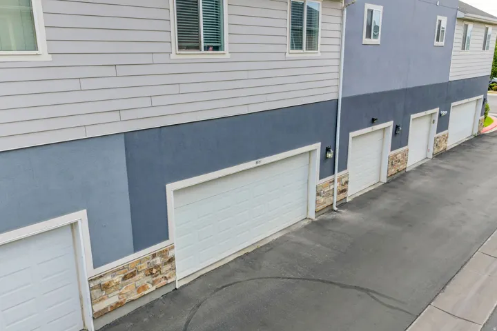 Multi-story residential facade featuring light gray horizontal siding, dark blue stucco, and stone veneer accents