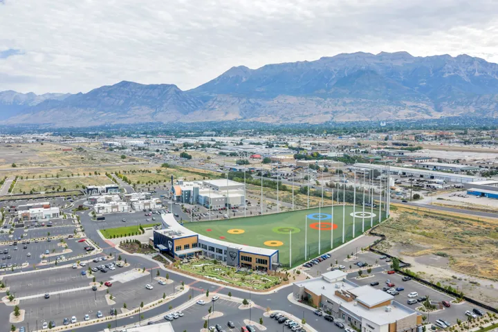Expansive aerial showcasing a recreational complex with a golf driving range, surrounding commercial buildings, and extensive parking areas