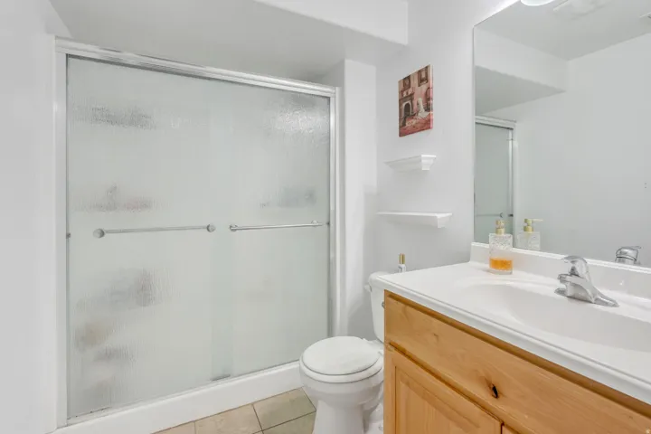 Bathroom featuring a frosted glass shower enclosure with sliding doors, a single-sink vanity with a light wood-finish cabinet, and a large wall-mounted mirror
