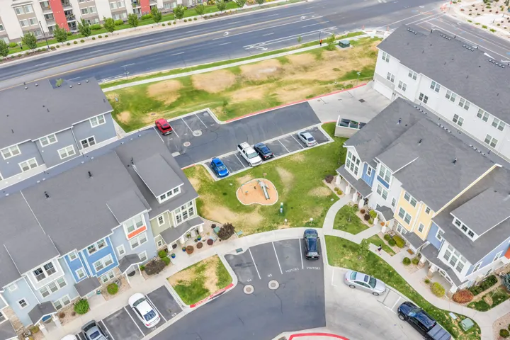 Community aerial showcasing townhomes with varied exterior siding colors, asphalt shingle roofs, dedicated parking areas, and a central green space with playground equipment