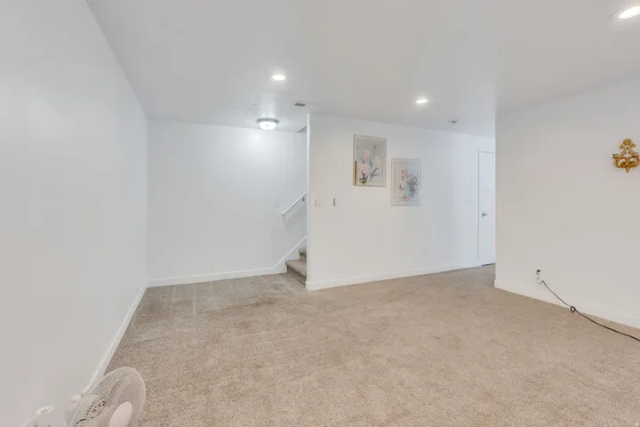 Carpeted room with white walls, recessed lighting, and a staircase