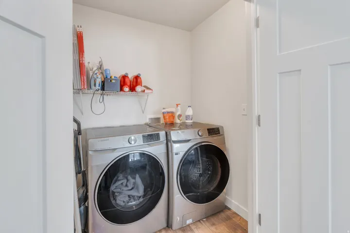 Dedicated laundry area featuring a front-loading washer and dryer, wood-finish flooring, and a wall-mounted wire shelf for storage