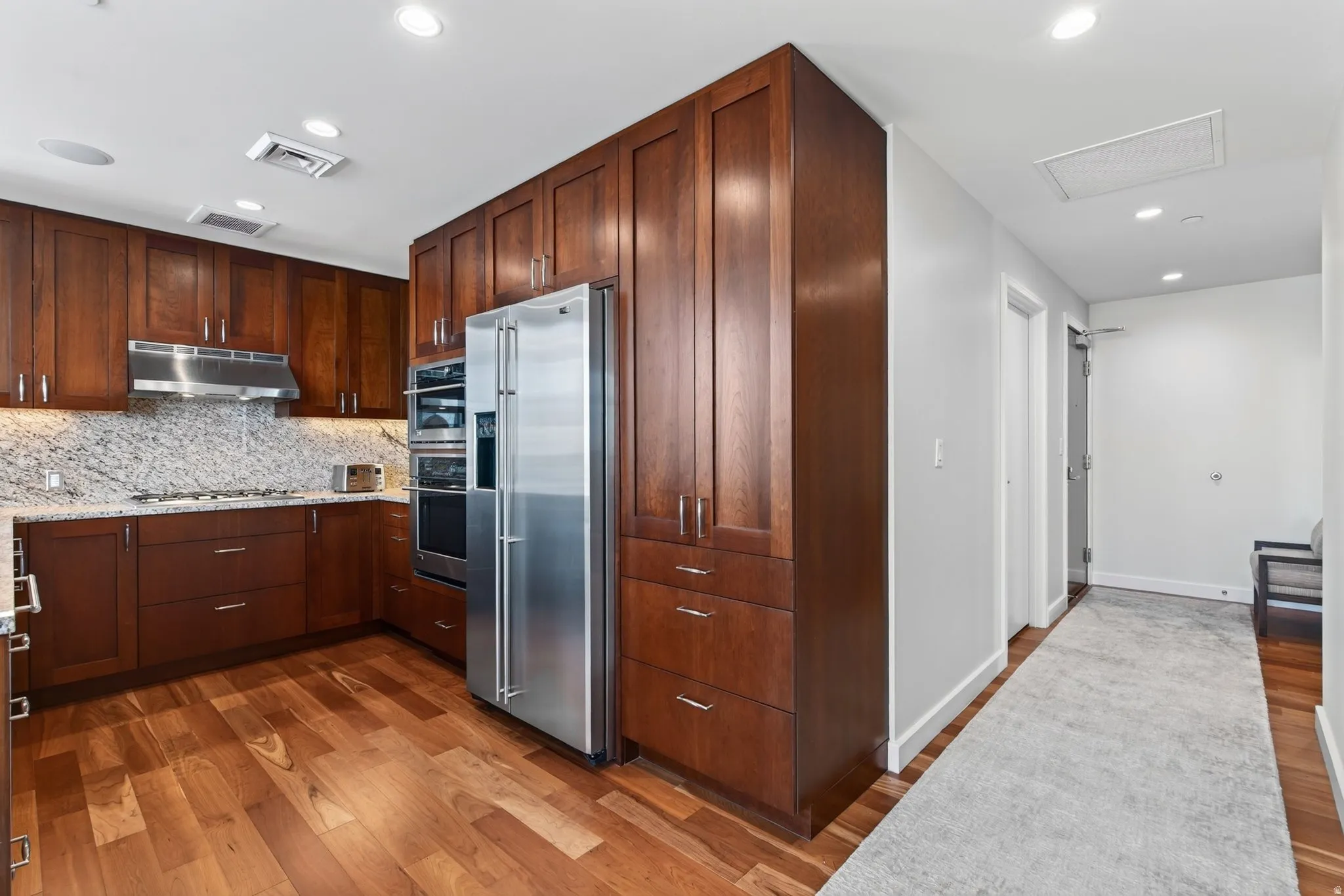 Kitchen featuring rich wood cabinetry, granite countertops, stainless steel appliances, and wood-finish flooring