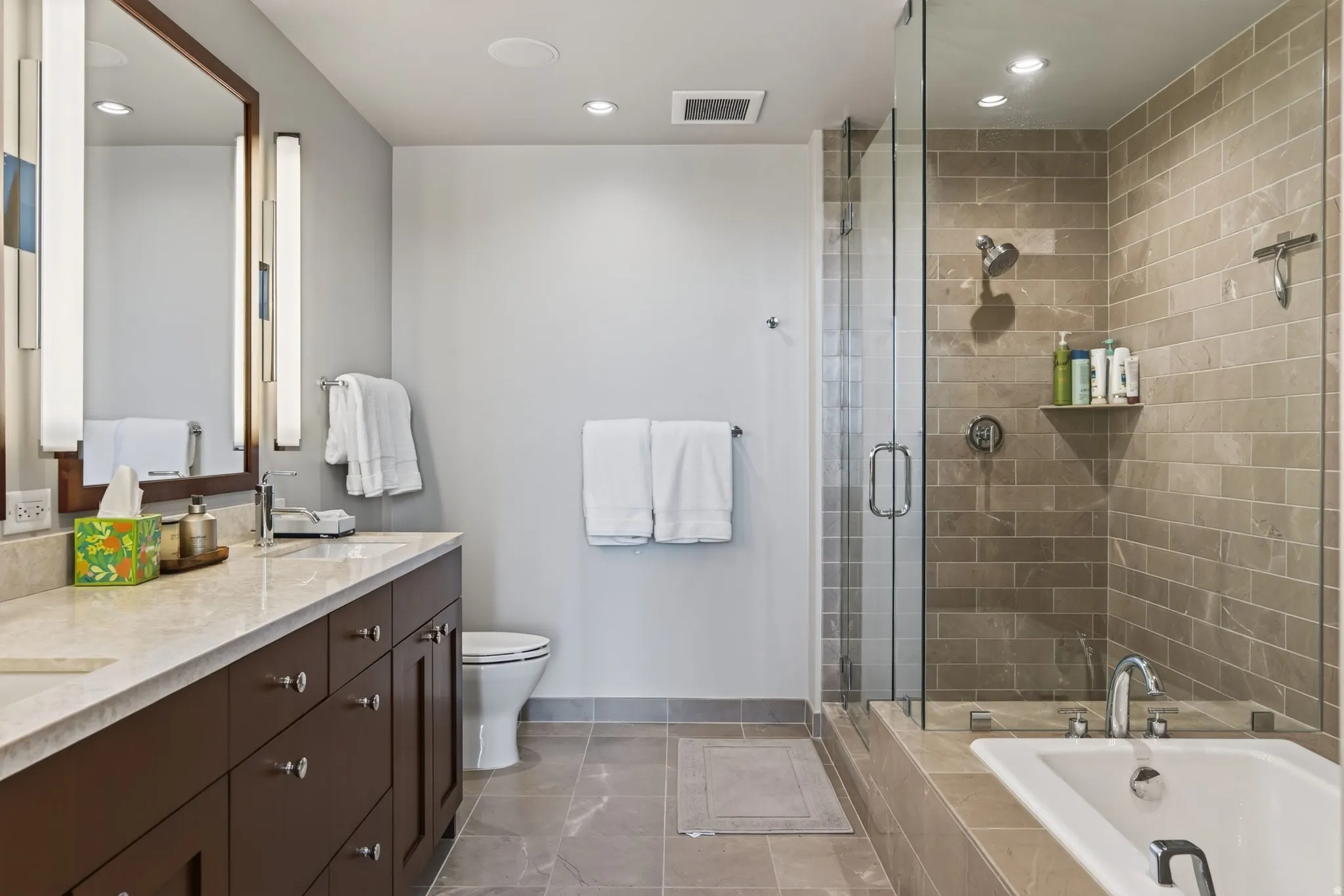 Bathroom featuring a double vanity with stone countertop, dark wood-finish cabinetry, and framed mirror with vertical sconces