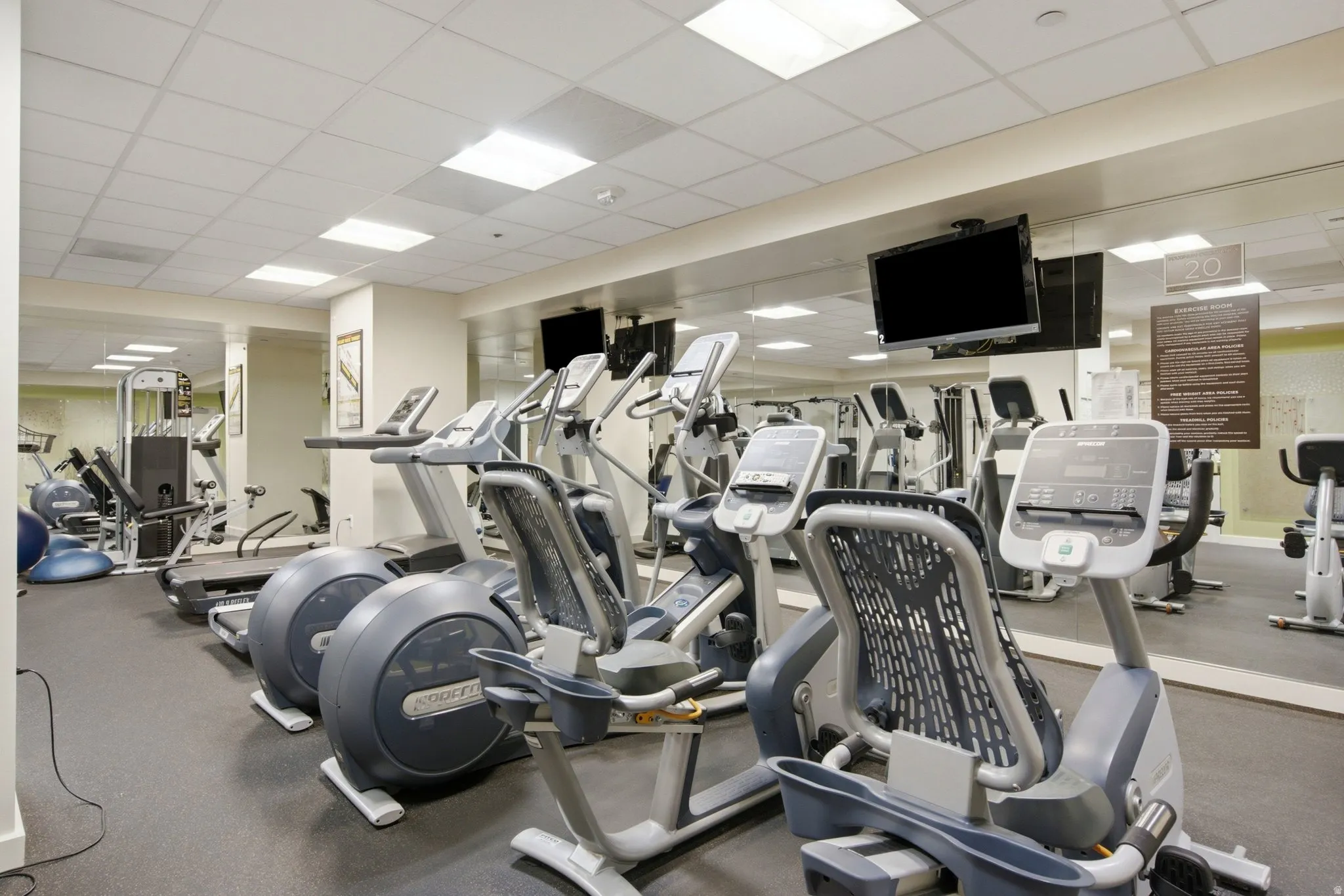 Fitness center featuring multiple exercise machines, mirrored walls, recessed lighting, and wall-mounted televisions