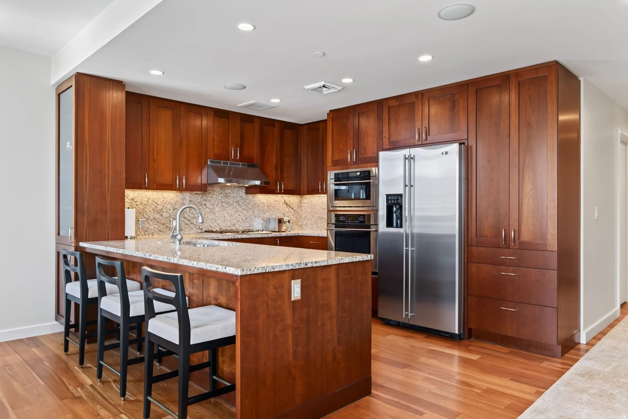 Kitchen featuring rich wood cabinetry, granite countertops, stainless steel appliances, and wood-finish flooring
