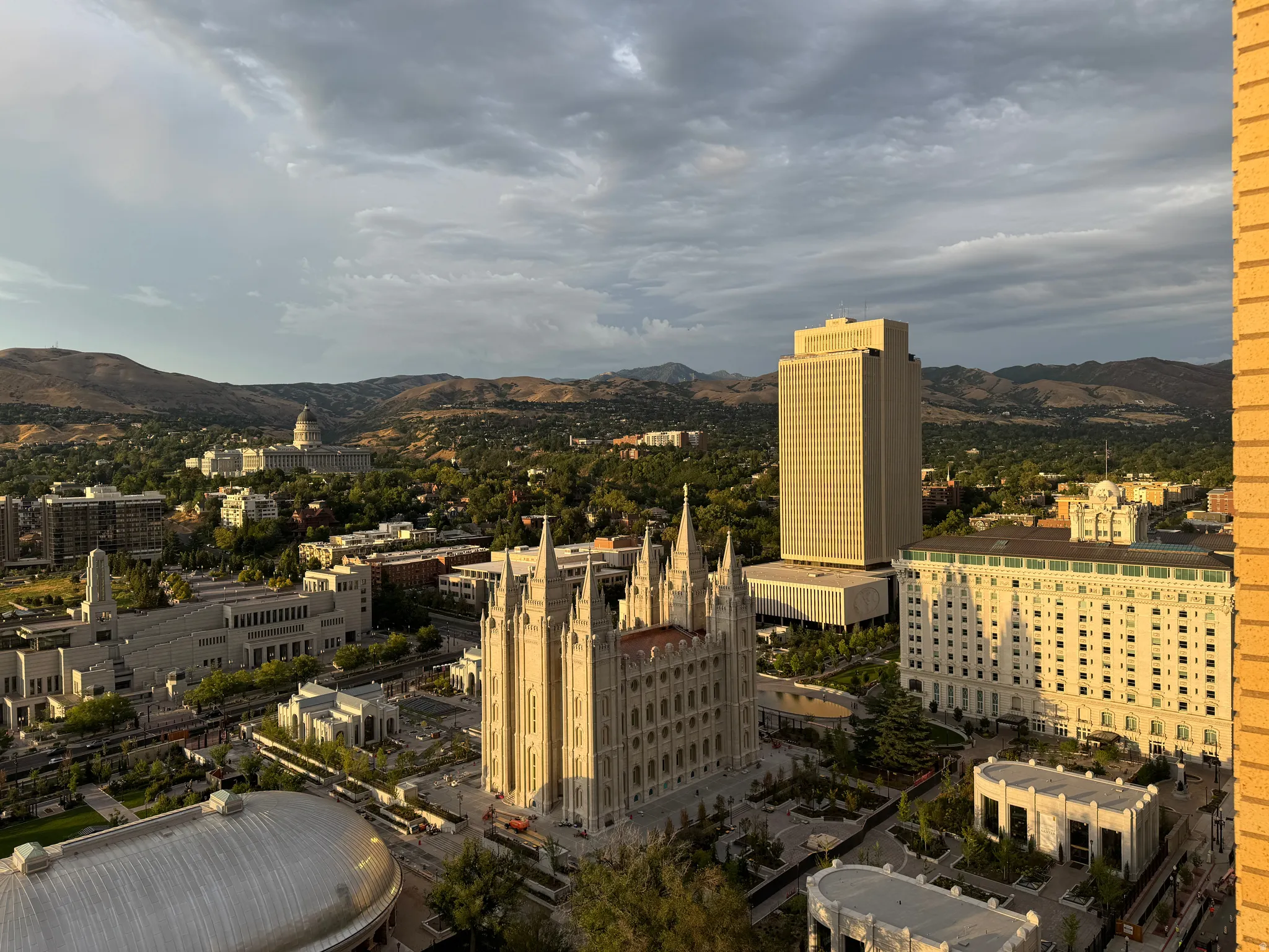 Expansive cityscape featuring prominent architectural landmarks, verdant tree-lined streets, and distant mountain ranges
