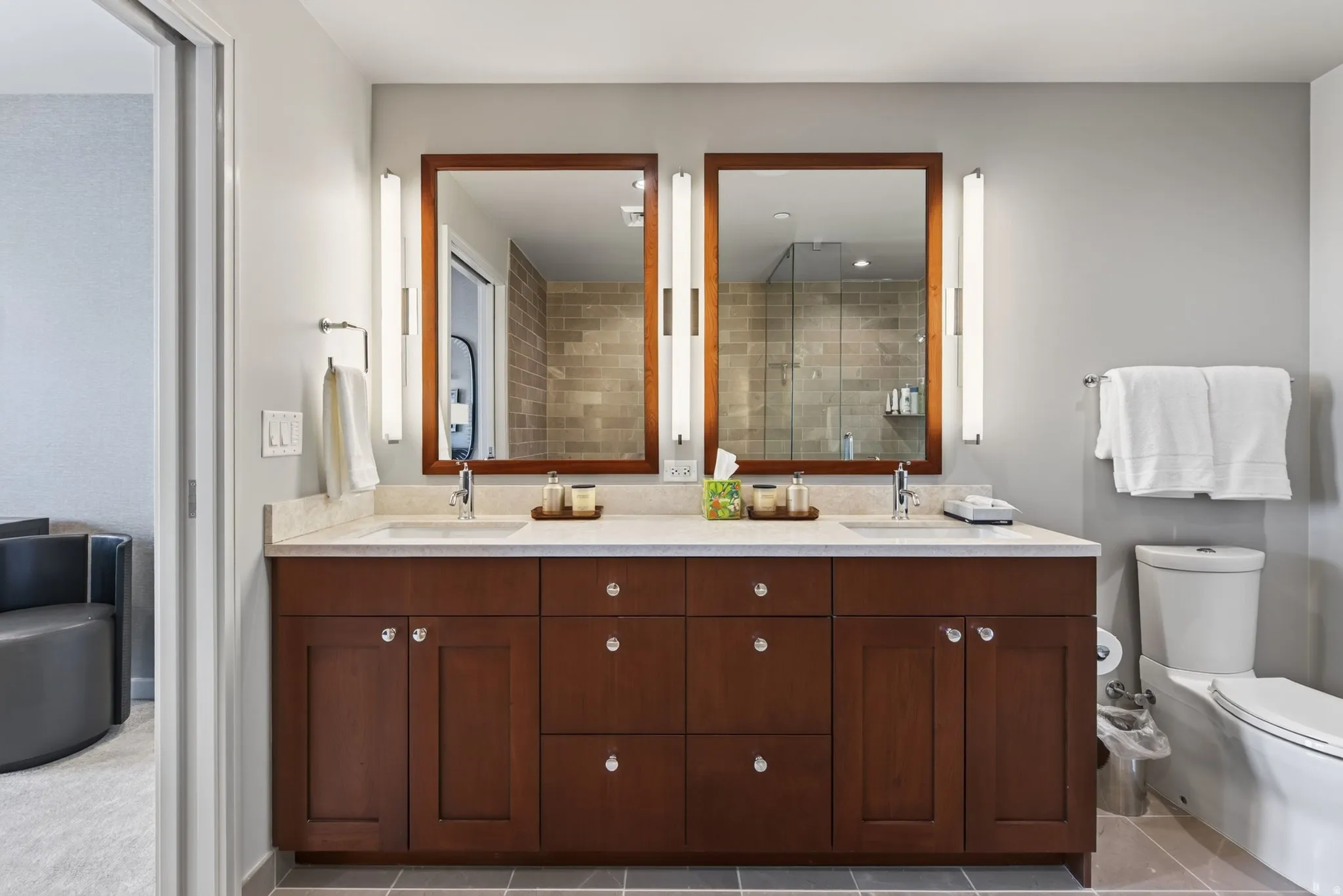 Dual vanity with stone countertop, integrated sinks, wood-finish cabinetry, and framed mirrors with vertical sconce lighting