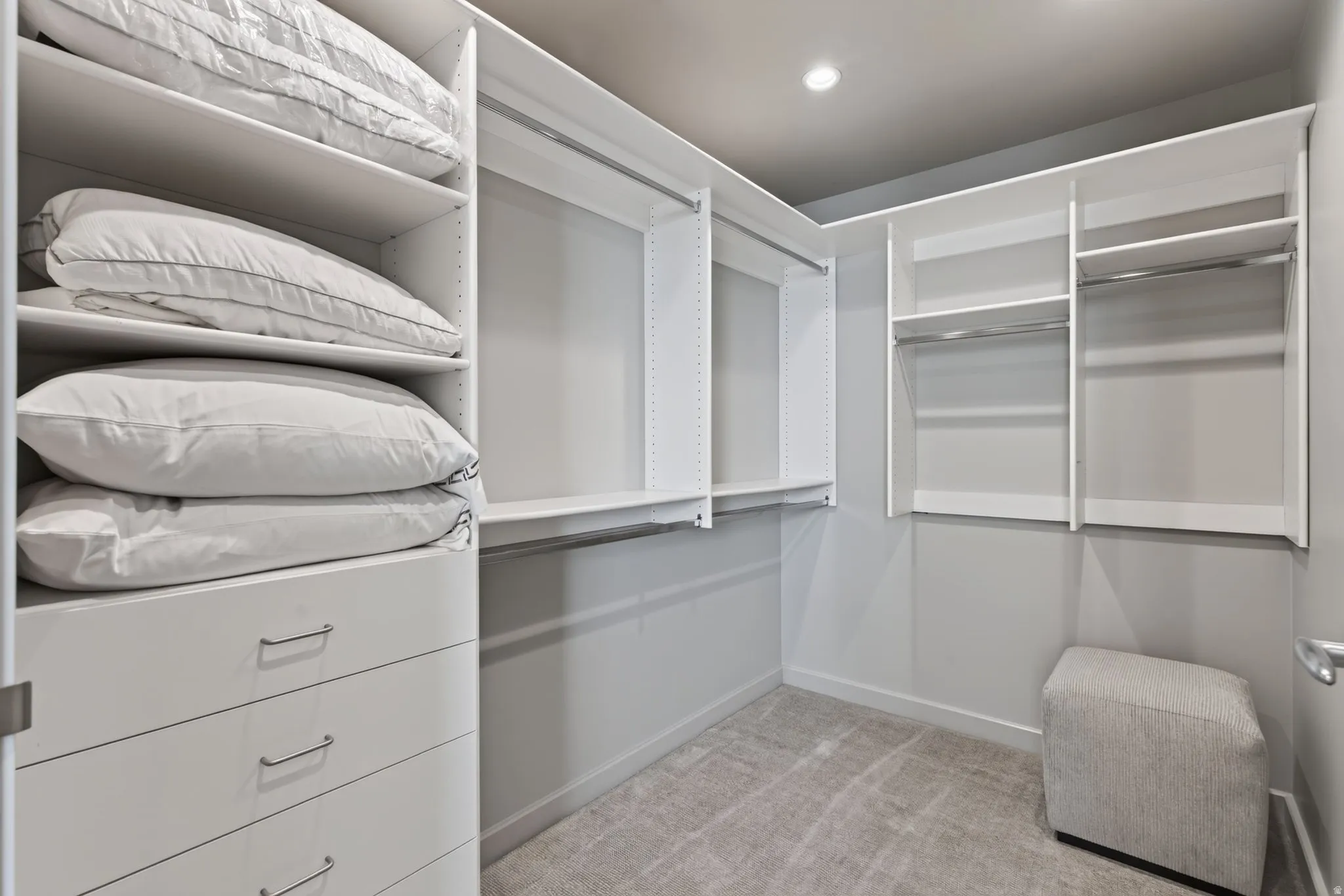 Custom closet system featuring white shelving units, multiple hanging rods, built-in drawers with modern hardware, and recessed ceiling lighting