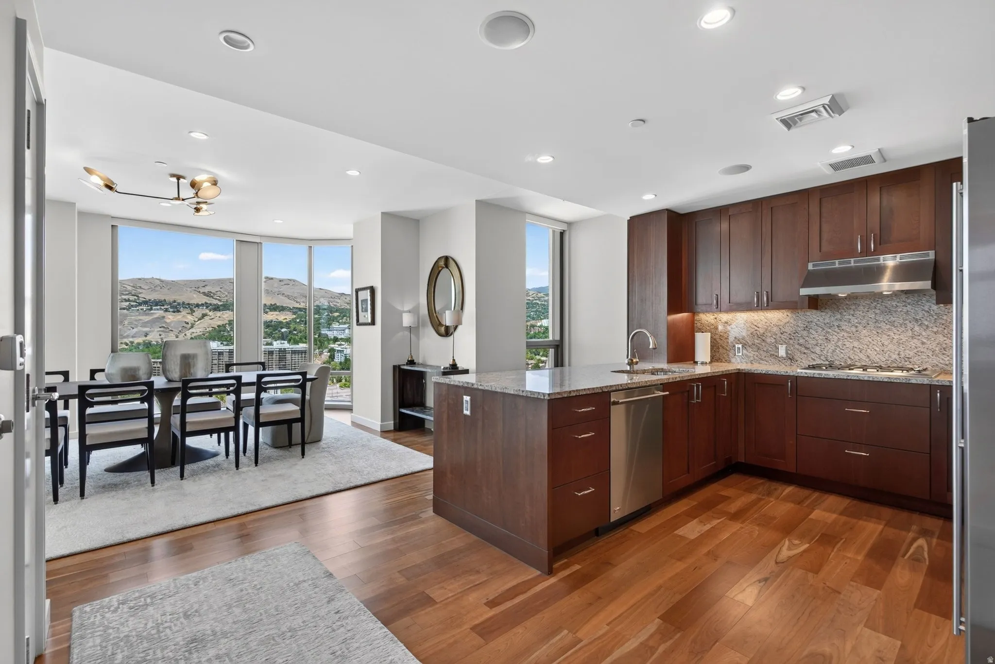 Gourmet kitchen featuring wood-finish flooring, dark wood cabinetry, stainless steel appliances, and stone countertops with a matching backsplash
