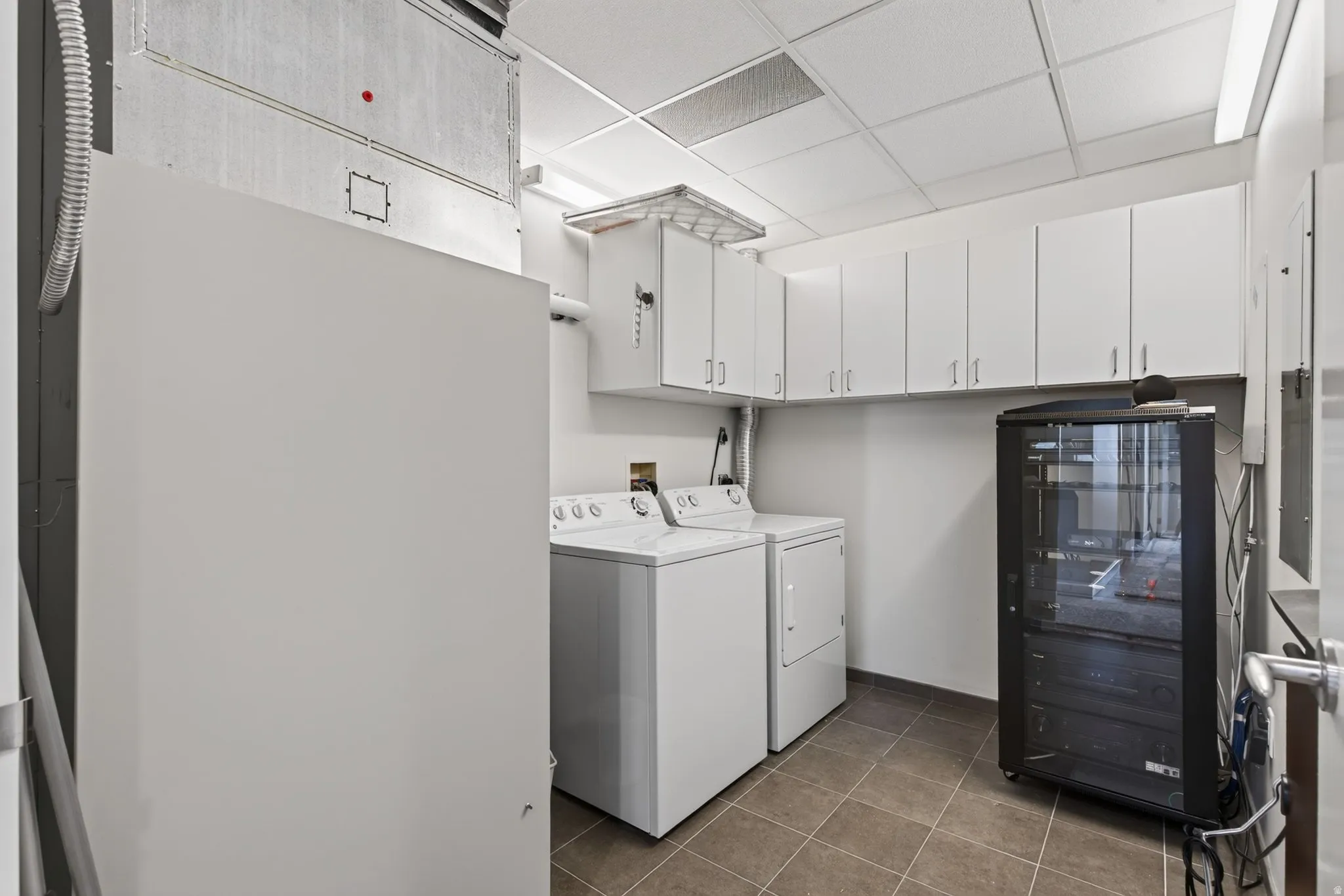Utility room featuring a washer and dryer, extensive white cabinetry, tile flooring, and a dropped ceiling with integrated lighting