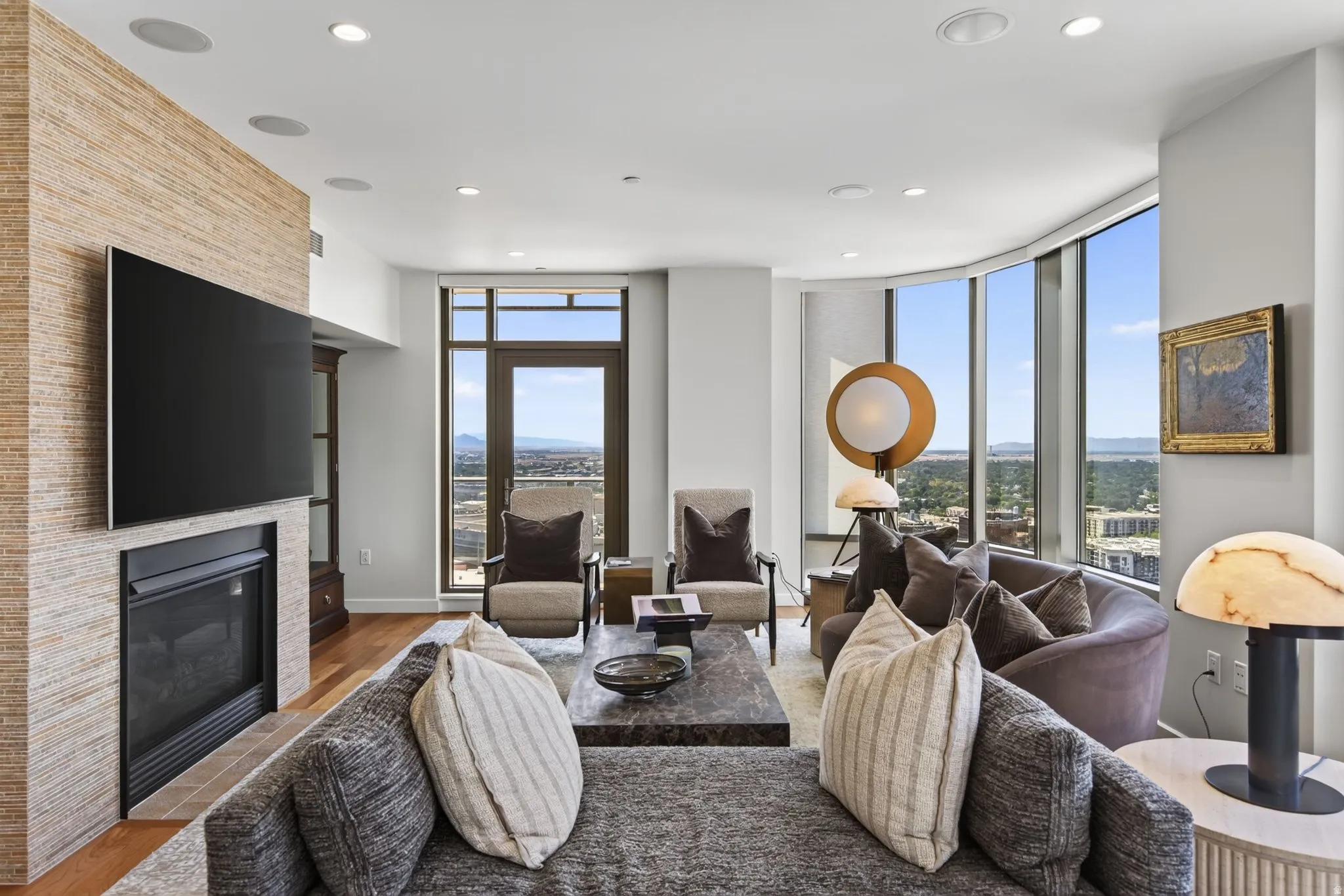 Living area featuring a textured accent wall, built-in fireplace, hardwood-finish flooring, and large curved windows