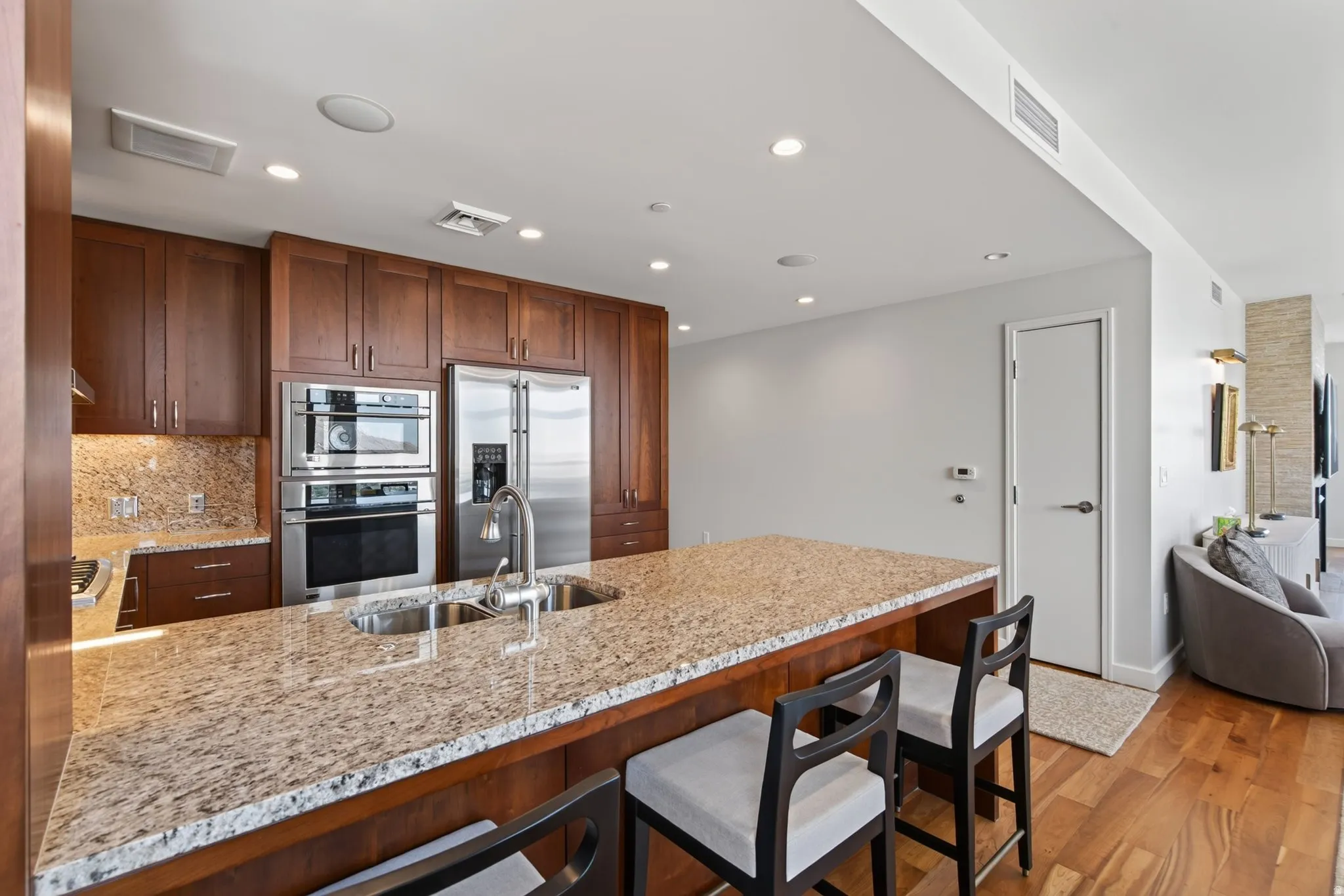 Expansive kitchen island with a double basin sink and granite countertop, rich wood cabinetry, stainless steel appliances, recessed lighting, and hardwood flooring