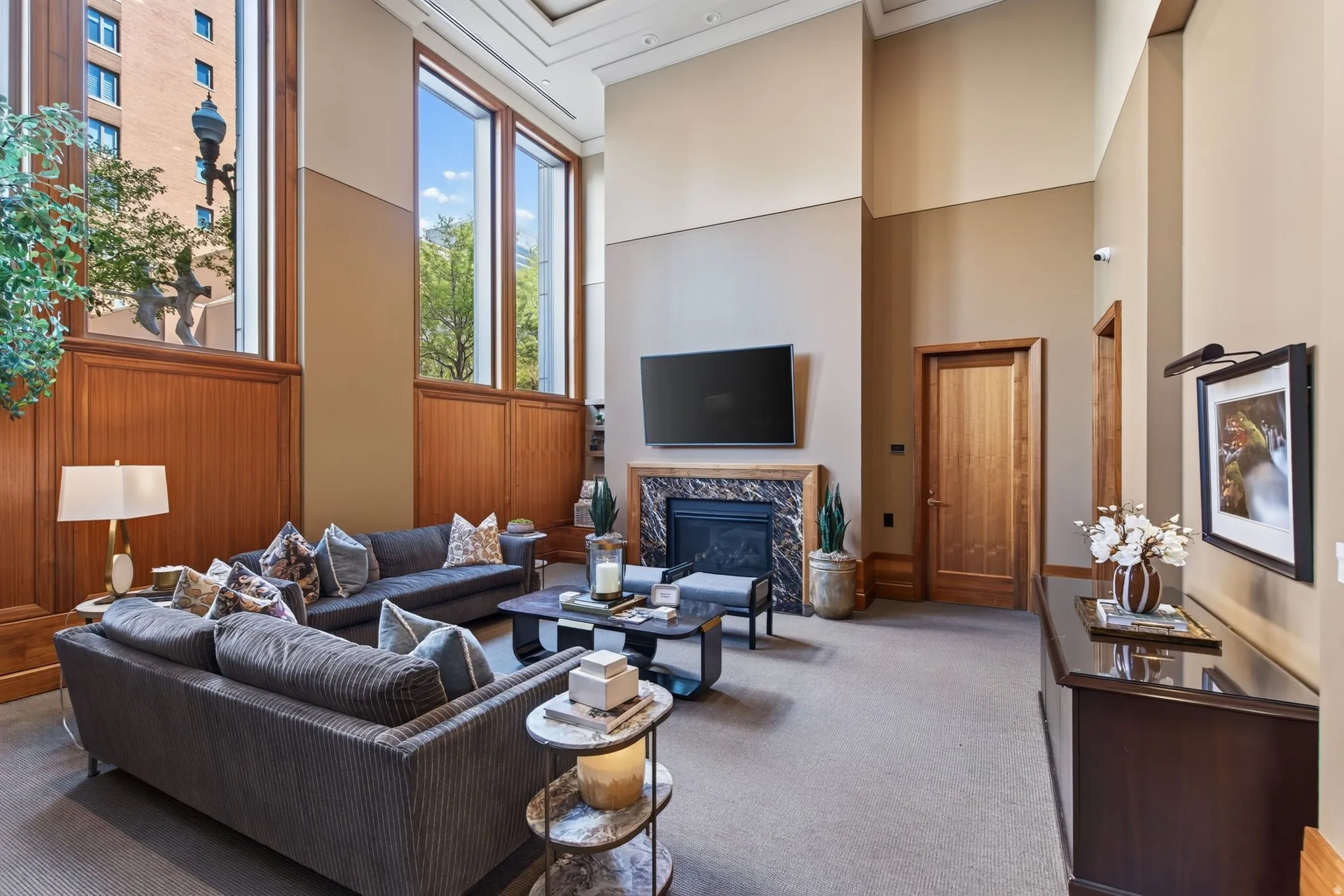 Spacious living area featuring double-height ceilings, a fireplace with a stone surround, and tall windows with wood paneling