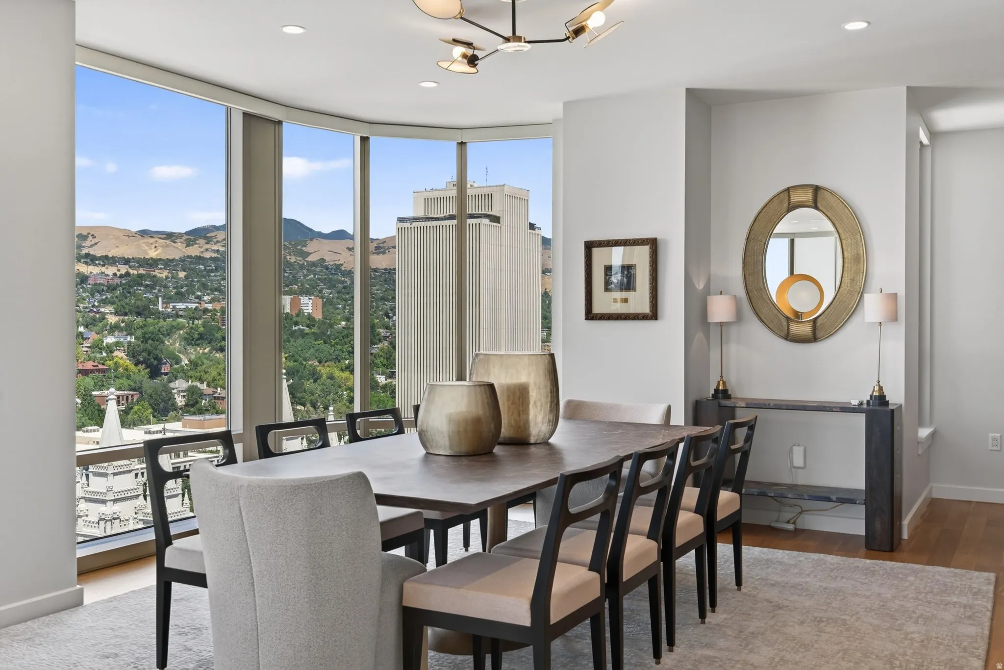 Dining area with extensive floor-to-ceiling windows, modern chandelier lighting, light wood-finish flooring, and a contemporary console table