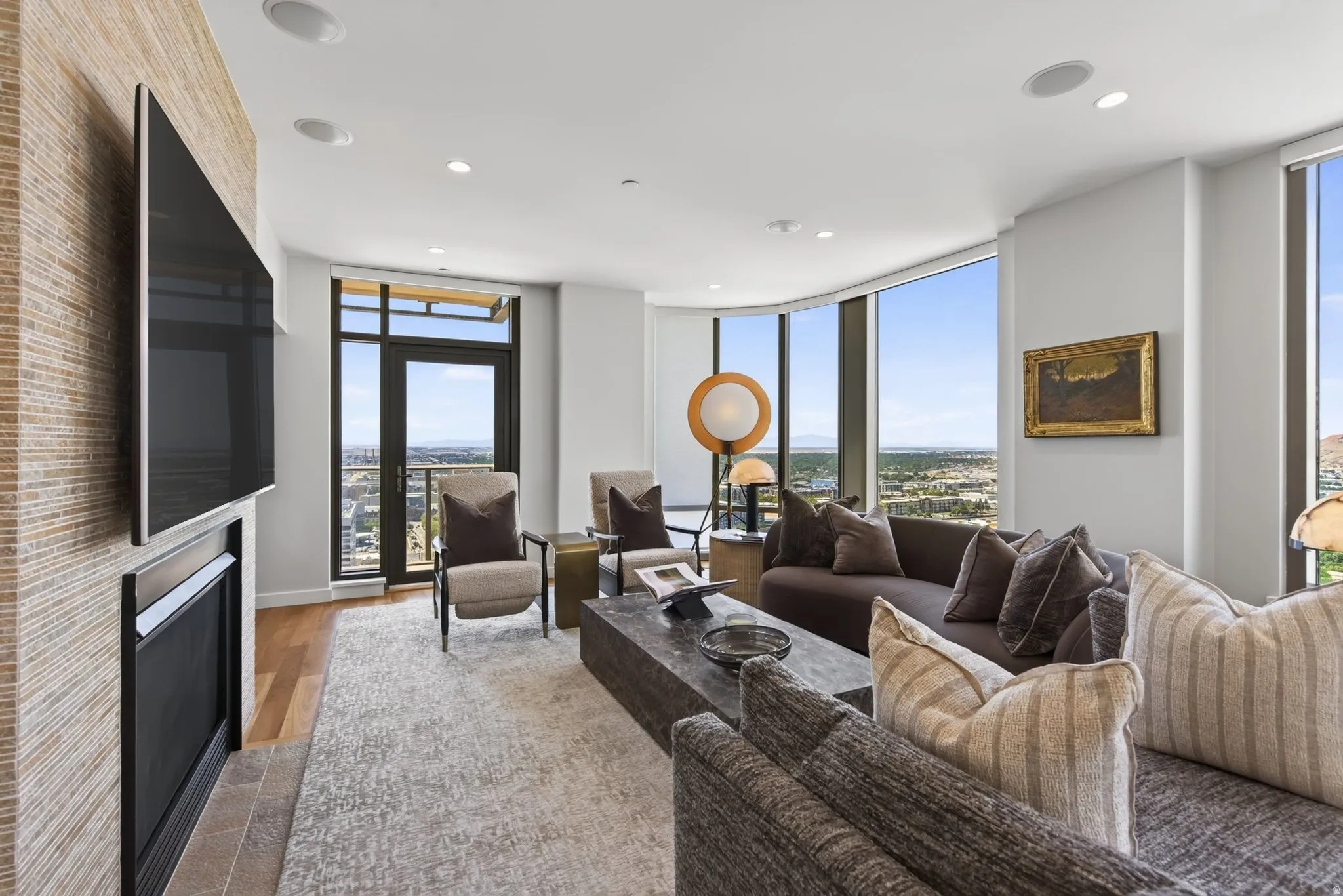 Living area featuring a contemporary fireplace with textured surround, floor-to-ceiling windows, recessed lighting, wood-finish flooring, and a glass-paneled door opening to an outdoor space