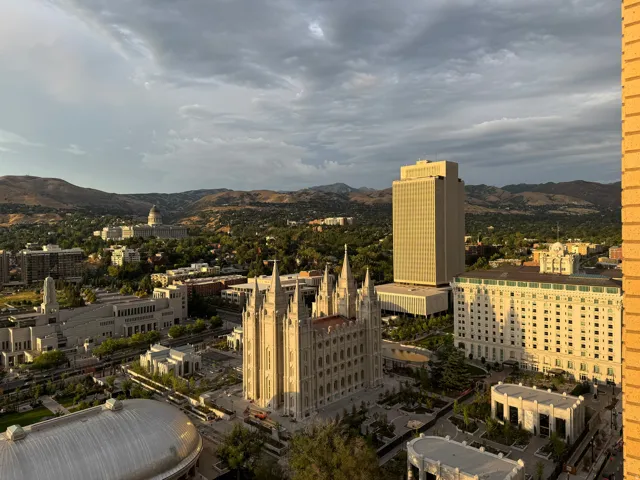 Expansive cityscape featuring prominent architectural landmarks, verdant tree-lined streets, and distant mountain ranges