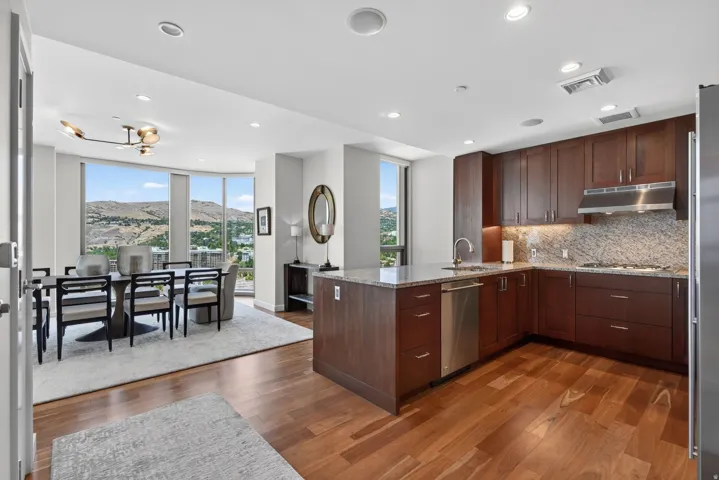 Gourmet kitchen featuring wood-finish flooring, dark wood cabinetry, stainless steel appliances, and stone countertops with a matching backsplash