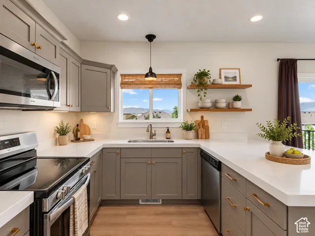 Modern kitchen featuring stainless steel appliances, grey cabinetry with gold-tone hardware, white countertops, and wood-finish flooring