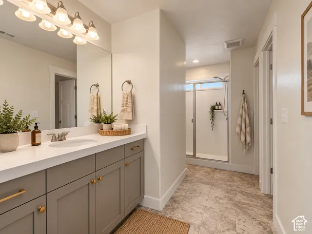 Recessed lighting with a glass-enclosed shower, a vanity featuring a white countertop with an undermount sink, and a multi-bulb vanity light fixture