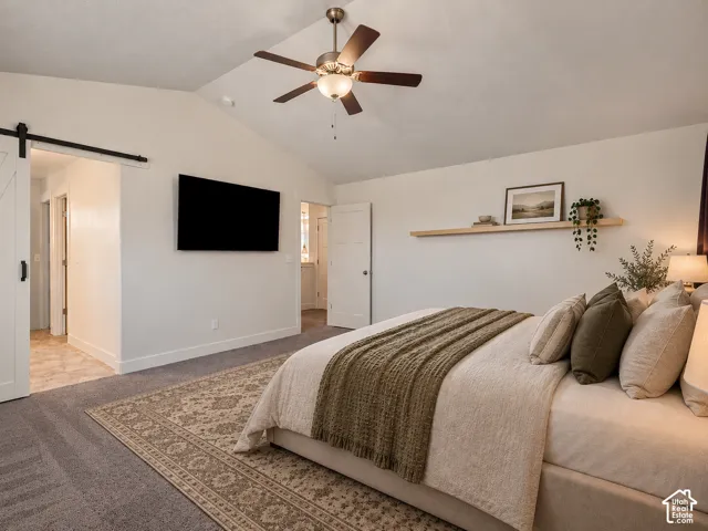 Vaulted ceiling with a ceiling fan, wall-mounted television, and a sliding barn door