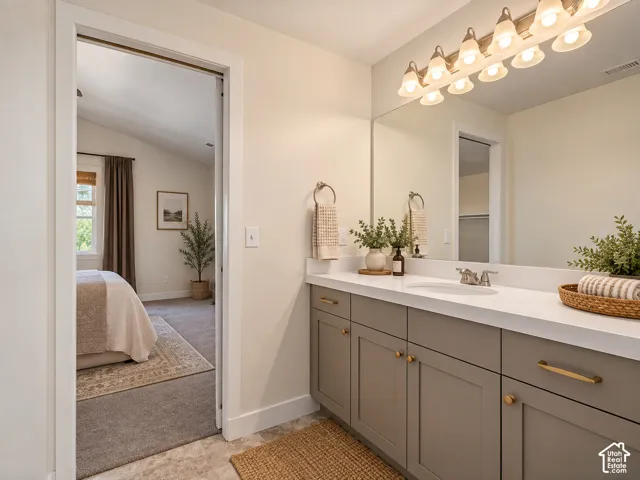 Vanity with a single basin, light-toned countertop, and gray cabinetry with gold-toned hardware
