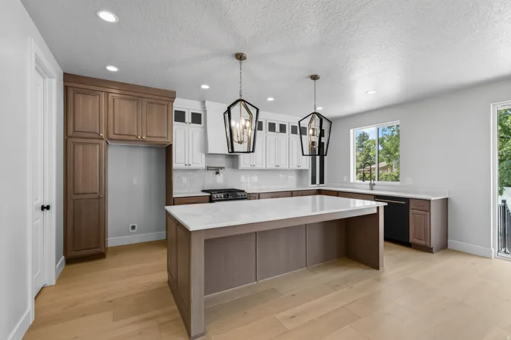 Two-tone cabinetry with contrasting finishes, a central island with a light-toned countertop, recessed lighting, and two geometric pendant lights